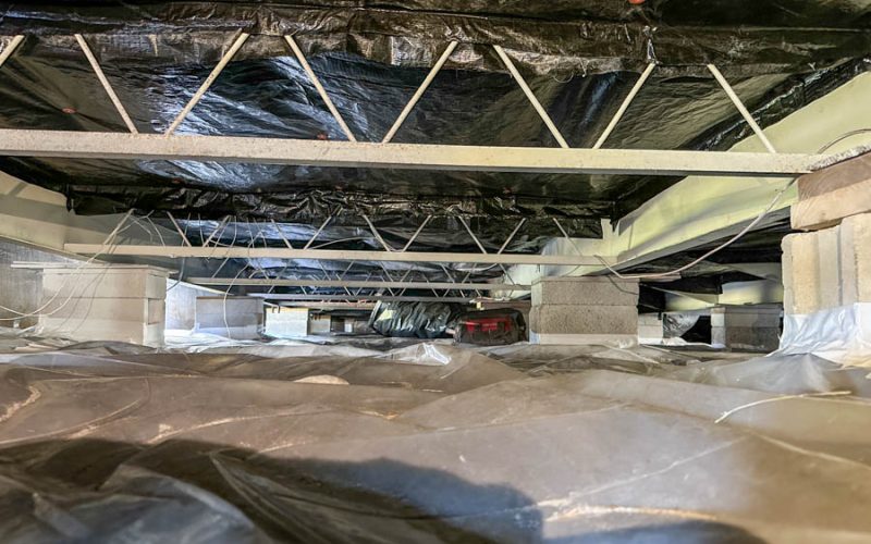 Completed East Coast Vapor Barrier installation showing a fully encapsulated crawl space with black vapor barrier lining the ceiling and floor, secured to joists and concrete piers for long-term moisture control.