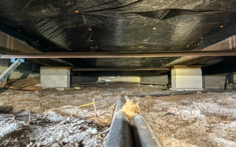 Raw crawl space floor with dirt, debris, and exposed utility lines before encapsulation — highlighting the need for East Coast Vapor Barrier’s moisture-proofing and structural protection services.