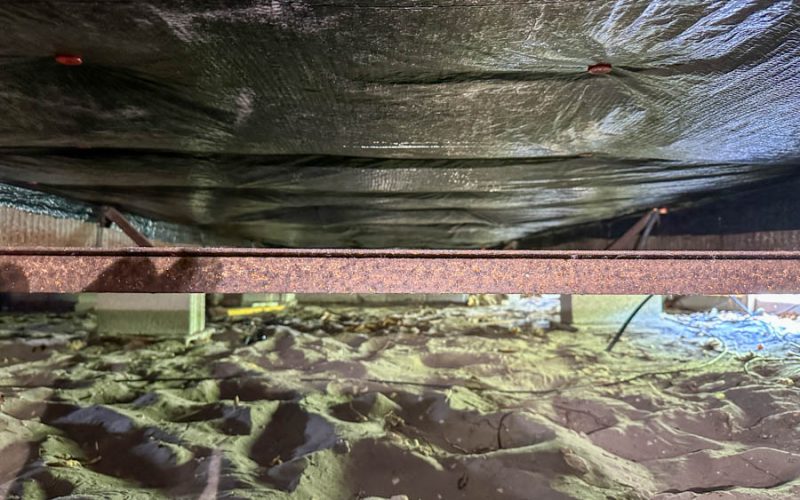Tight seal between black vapor barrier and rusty steel beam, secured with orange fasteners — highlighting the precision installation that prevents air and moisture leaks in the crawl space ceiling.