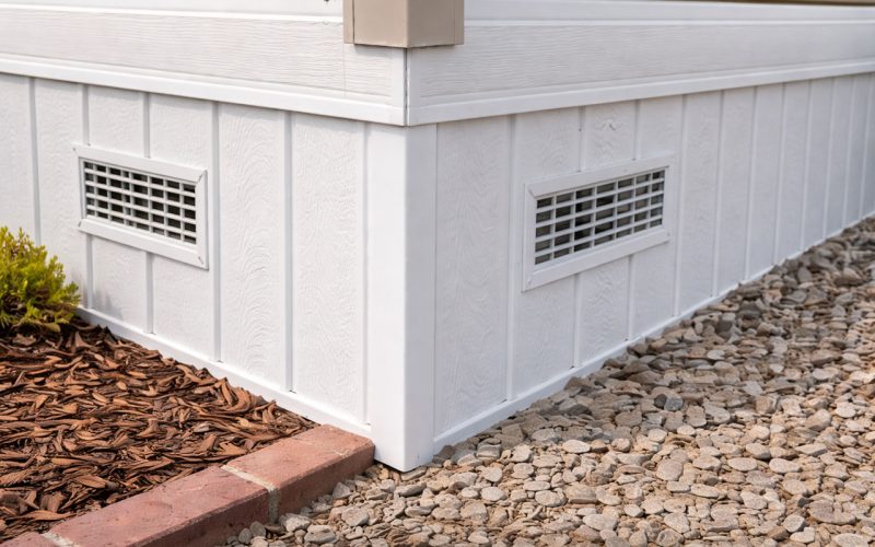 Clean, white vinyl skirting installed along the perimeter of a home’s foundation, featuring built-in ventilation grilles to promote airflow while protecting the crawl space from pests and weather.